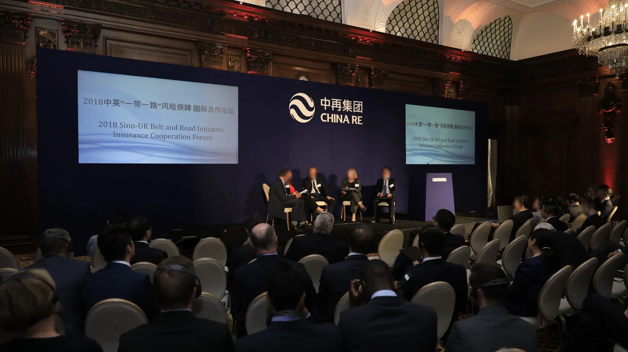 A panel discussion on stage between screens carrying the forum title