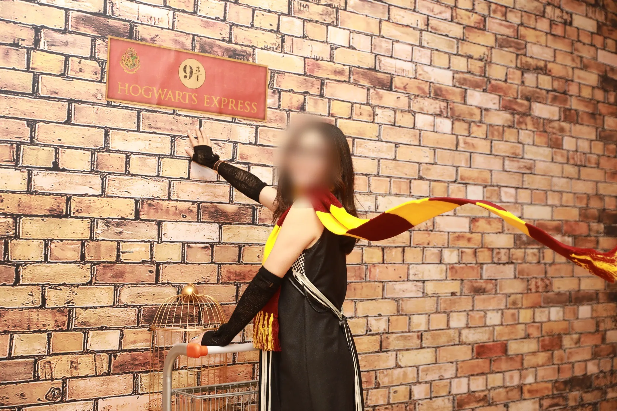 A guest in costume posing at a themed railway platform set built against a brick wall