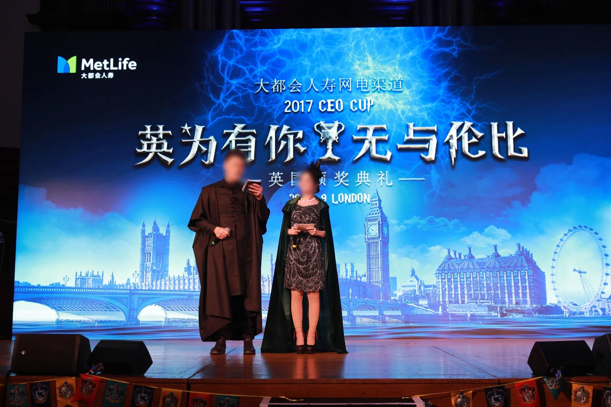Hosts on stage in costume in front of a London skyline backdrop carrying the event theme