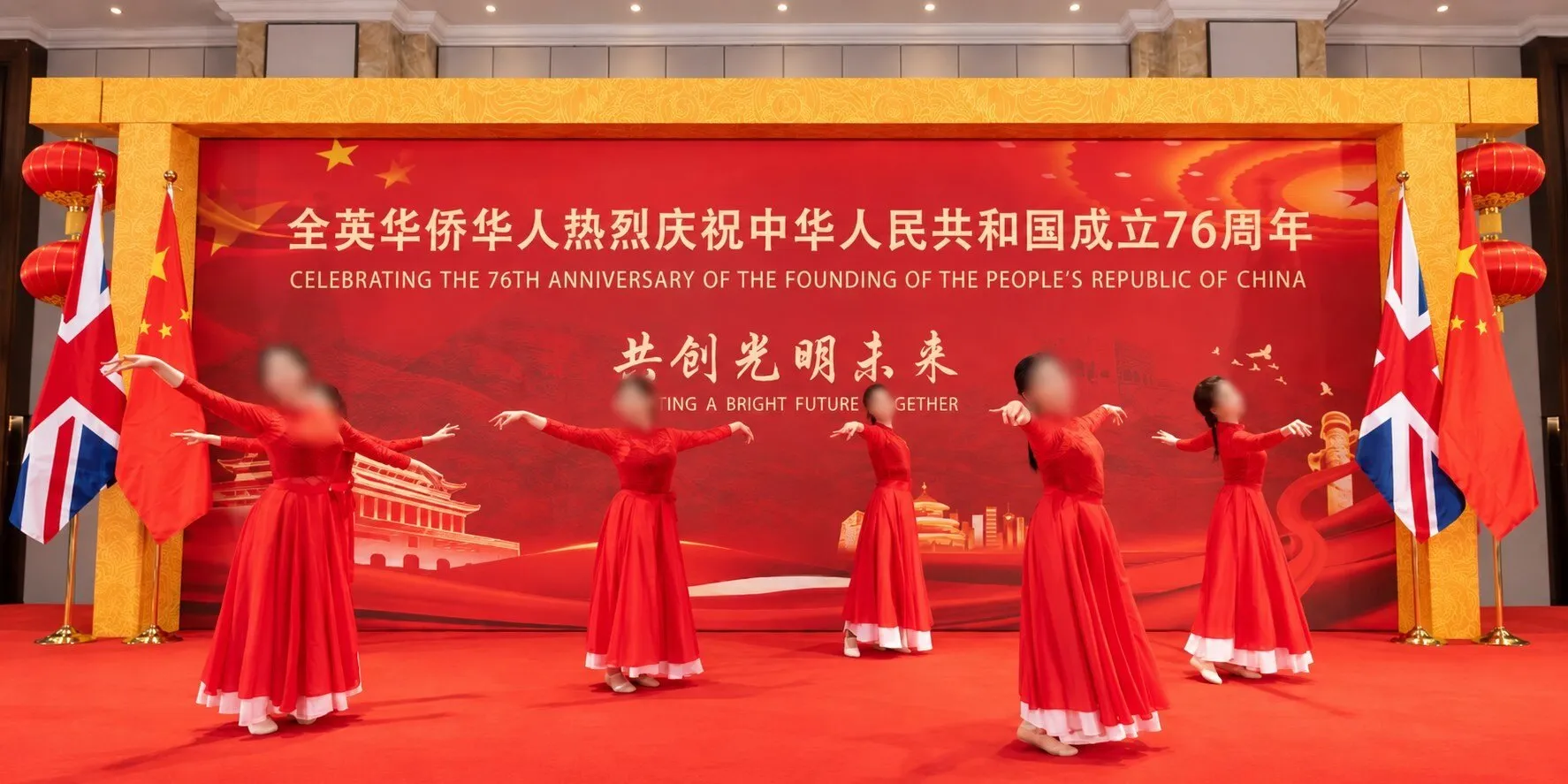 Dancers in red dresses performing in front of the celebration backdrop, between British and Chinese flags