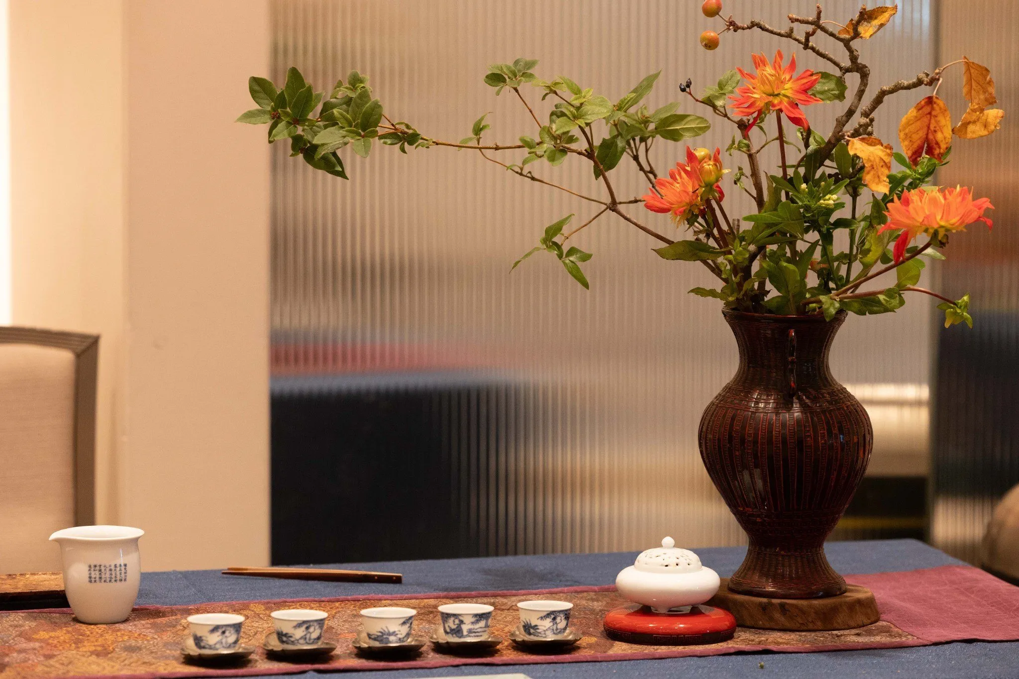 A traditional tea culture display with a row of tea cups, an incense burner and a vase of autumn flowers